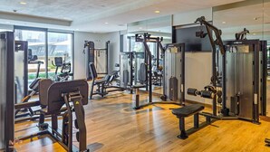 Ein Fitnessstudio mit verschiedenen Trainingsgeräten, großen Fenstern und Holzboden.