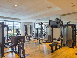 A gym with various exercise machines, large windows, and a wooden floor. - Madely | Chic Act One Haven | Burj Khalifa (Dubai)