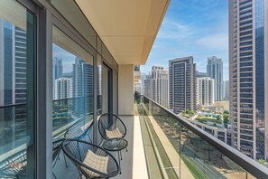 A balcony with a view of high-rise buildings, two wicker chairs, and a glass railing. - Madely | Chic Act One Haven | Burj Khalifa (Dubai)