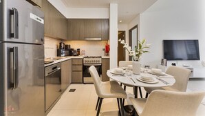 Eine moderne Küche mit Edelstahlgeräten, einem Essbereich mit rundem Tisch und Stühlen sowie einem wandmontierten Flachbildfernseher.