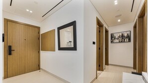 A hallway with wooden doors, a mirror, and a cityscape painting on the wall. - Madely | Stylish 2BR with Private Pool (Dubai)