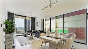 A modern living room with a dining area, large windows, and a view of the cityscape. - Madely | Stylish 2BR with Private Pool (Dubai)