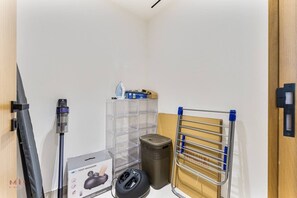 A small room with a vacuum cleaner, a foot massager, a storage unit, and a drying rack. - Madely | Stylish 2BR with Private Pool (Dubai)