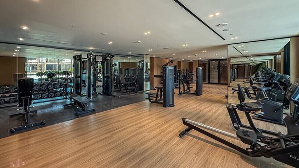 A gym with various exercise equipment, including treadmills and weight machines, and a wooden floor. - Madely | Stylish 2BR with Private Pool (Dubai)