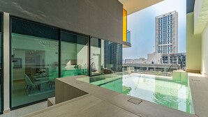 A modern interior with a glass-enclosed dining area, a pool, and a view of surrounding buildings. - Madely | Stylish 2BR with Private Pool (Dubai)