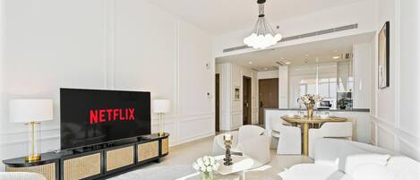 A modern living room with a flat-screen TV displaying 'NETFLIX,' a sofa, a coffee table with a vase, and a dining area with a round table and chairs.