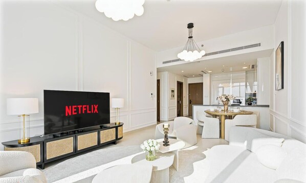 Ett modernt vardagsrum med en platt-TV som visar "NETFLIX", en soffa, ett soffbord med en vas och en matplats med ett runt bord och stolar.