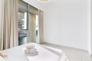 Une chambre d’hôtel avec une grande fenêtre, un lit sur lequel est posée une serviette roulée, et une vue sur un port de plaisance.