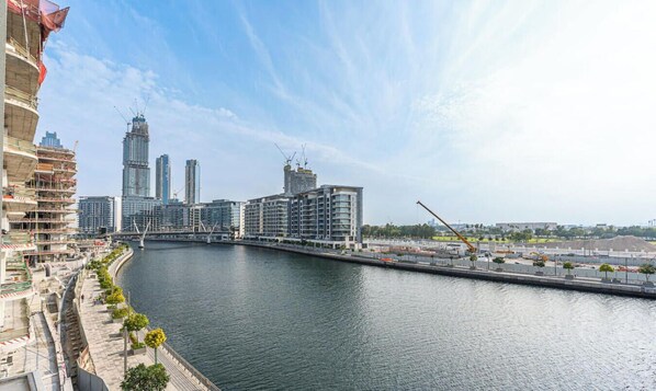 A river with modern buildings, a bridge, and a construction crane. - Canal-Side Living  Elegant 2BR in Canal Front (Dubai)