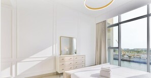 A hotel room with a large window, a bed, a dresser, and a mirror. - Canal-Side Living  Elegant 2BR in Canal Front (Dubai)