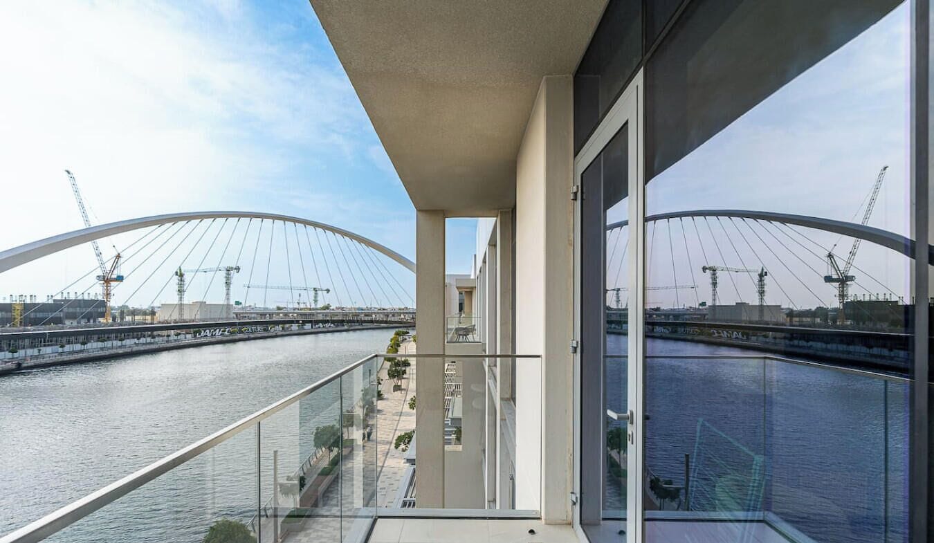 A modern building with a glass balcony overlooking a river and a bridge under construction.