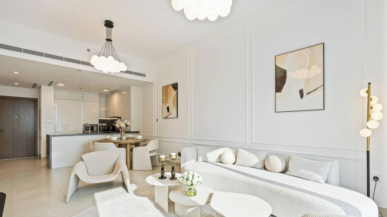Una sala de estar moderna con sofá, sillas, una mesa de centro y un comedor con una cocina al fondo.