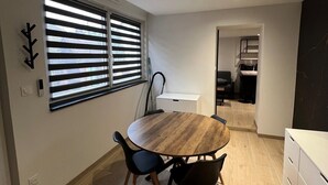 Una cucina moderna con tavolo e sedie in legno, una finestra con persiane e vista sull'area soggiorno adiacente.