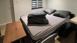 Una stanza compatta con un letto, un piccolo tavolo di legno e una finestra con persiane.