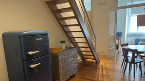 Eine Küche mit einer Holztreppe, einem Kühlschrank, einem Holzes Esstisch mit Stühlen und einem Fenster.
