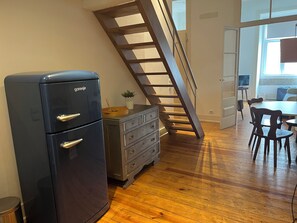 Eine Küche mit einer Holztreppe, einem Kühlschrank, einem Holzes Esstisch mit Stühlen und einem Fenster.