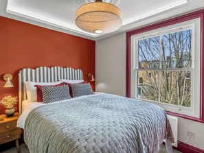 Een slaapkamer met een groot bed, een raam met uitzicht, een plafondlamp en een nachtkastje met een lamp.