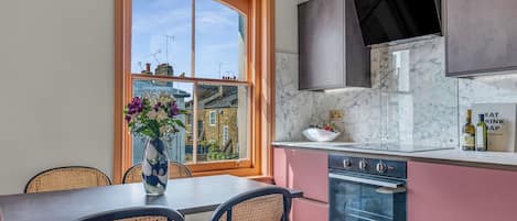 A kitchen with a large window, a dining table with chairs, a stove, and cabinets.