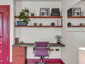 Een kamer met een bureau, planken, een stoel en een rode deur.