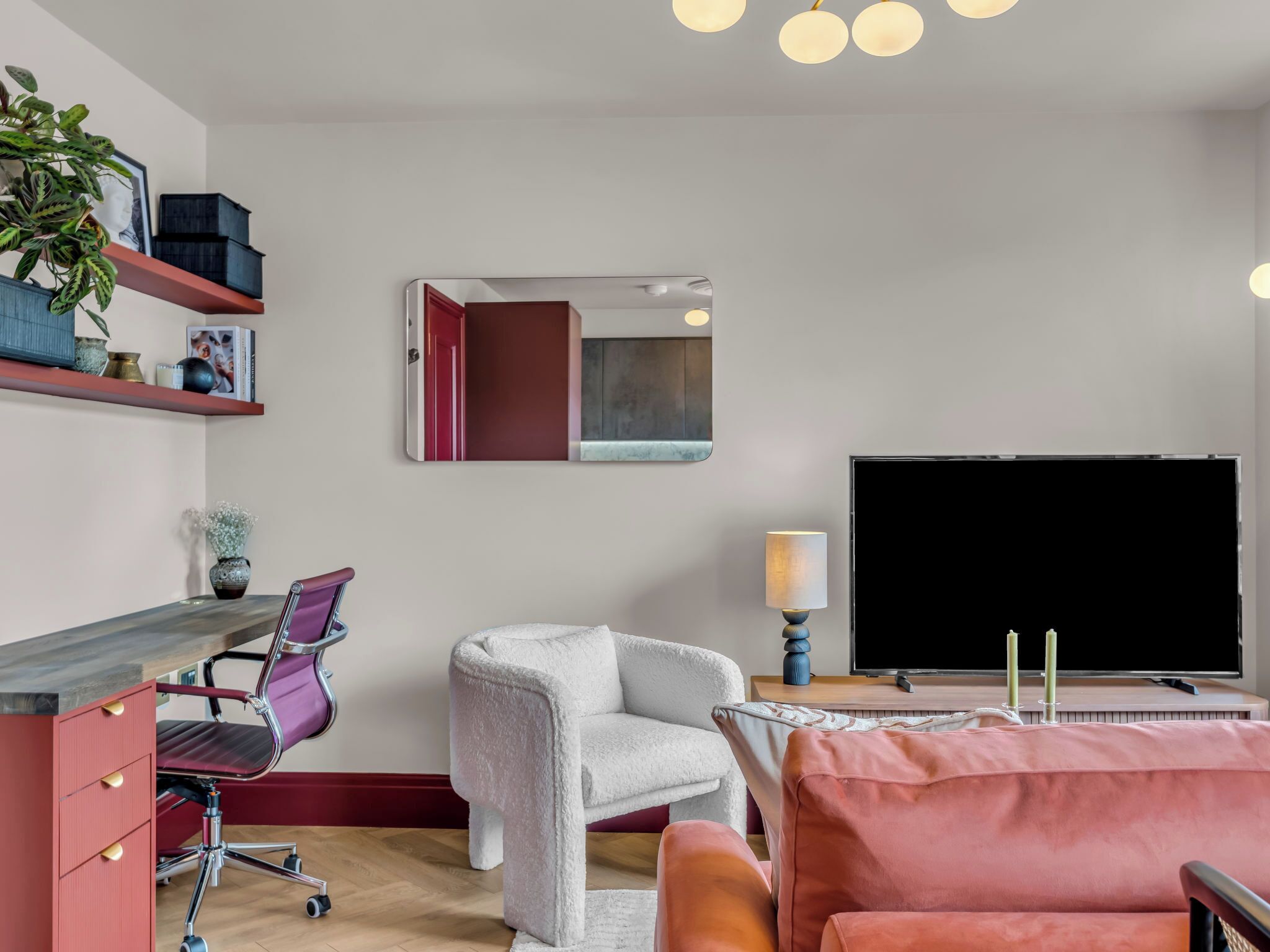 A modern living room with a flat-screen TV, a sofa, a chair, a desk, and a mirror.