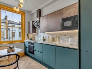 Uma cozinha moderna com armários verde-água, micro-ondas preto e vista para um edifício.