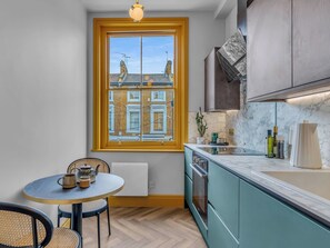 Une cuisine moderne avec des armoires de couleur turquoise, un comptoir en marbre, une fenêtre donnant sur des immeubles, une table ronde avec des chaises et un luminaire suspendu.