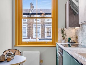 A kitchen with a large window, a round table with tea sets, and a view of a brick building. - London West Retreat 2 by Interhome (London West End)