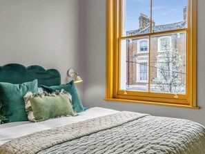 Une chambre à coucher avec un lit, des oreillers, une lampe et une fenêtre donnant sur des immeubles.