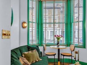 Um quarto com um sofá verde, uma mesa redonda com cadeiras e uma janela com persianas verdes.