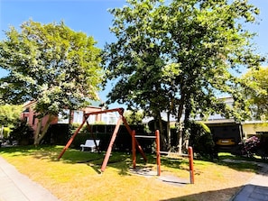 Un parque infantil con columpios y un tobogán, rodeado de árboles y césped.