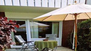 A patio with a table, chairs, and an umbrella. - Apartment 'Nordlicht' with Private Terrace, Garden, and Wi-Fi (Borkum)