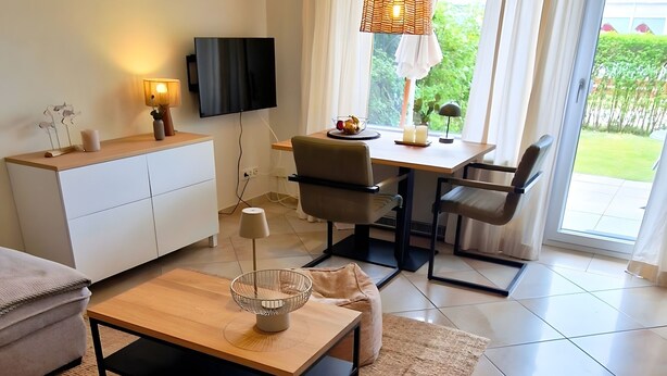 A modern living room with a sofa, coffee table, TV, and dining area. - Apartment 'Nordlicht' with Private Terrace, Garden, and Wi-Fi (Borkum)