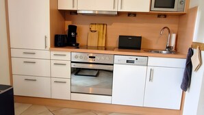 A compact kitchen with white cabinets, a microwave, an oven, and a dishwasher. - Apartment 'Nordlicht' with Private Terrace, Garden, and Wi-Fi (Borkum)