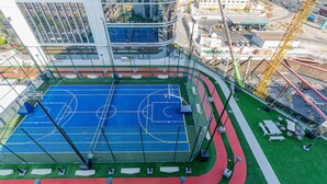 Een basketbalveld buiten met een groene omgeving, een rode atletiekbaan en een uitzicht op een stadsbeeld.