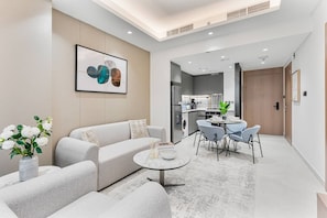 A modern living room with a sofa, coffee table, and chairs, a kitchen in the background, and a framed artwork on the wall. - Luxury 1BR Retreat w/ Balcony | JVT (Dubai)