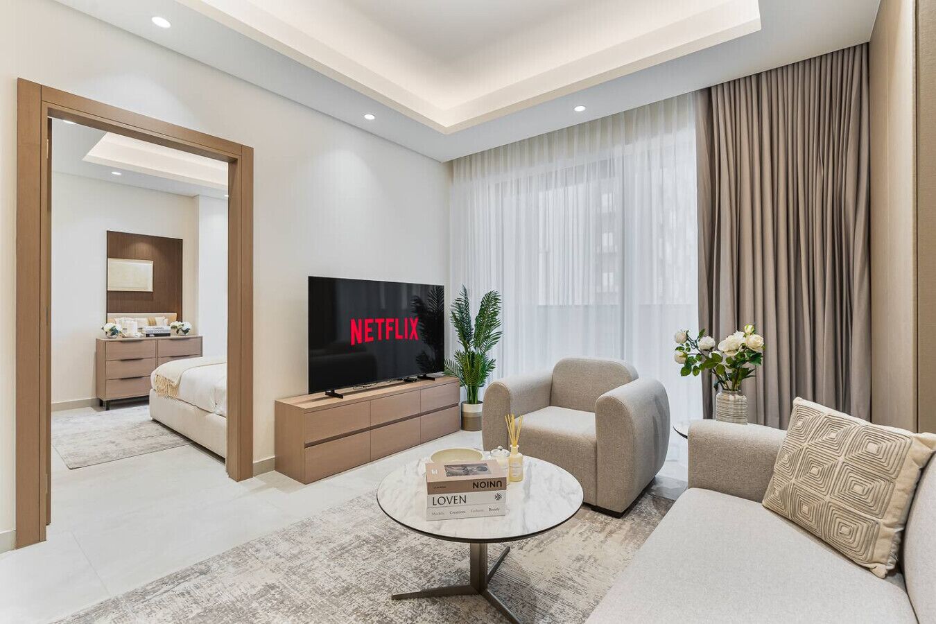Una sala de estar moderna con una televisión de pantalla plana, un sofá, una mesa de centro y un comedor con una mesa y sillas.