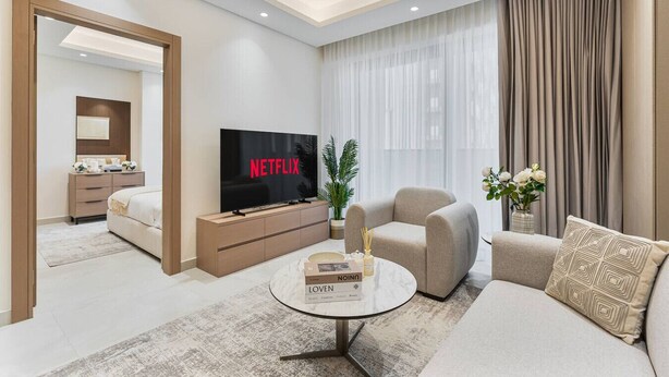 Een moderne woonkamer met een flatscreen televisie, een bank, een salontafel en een eethoek met tafel en stoelen.
