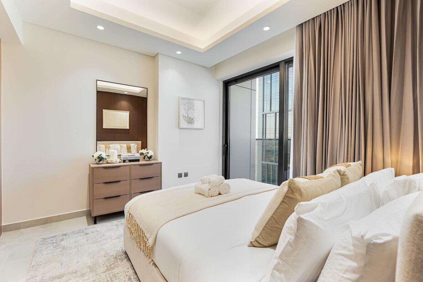 Quarto de hotel moderno com uma cama grande, penteadeira, espelho e janela com cortinas.