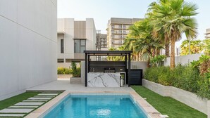 A modern outdoor pool area with a built-in bar, surrounded by greenery and palm trees. - Spacious | 4 Bed Villa | Private Pool | Meydan (Dubai)