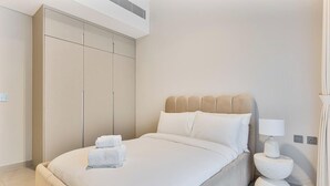 A hotel room with a bed, a wardrobe, a bedside table with a lamp, and a wall socket. - Spacious | 4 Bed Villa | Private Pool | Meydan (Dubai)