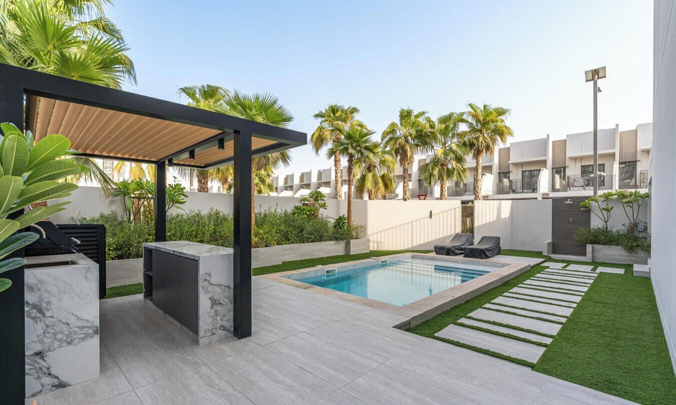 A modern outdoor pool area with a pergola, palm trees, and a well-maintained lawn.