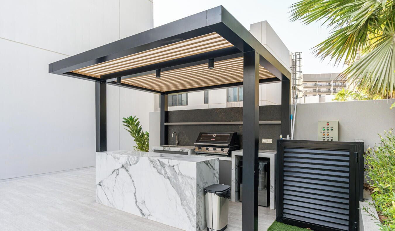 An outdoor kitchen with a marble countertop, a grill, and a pergola structure.