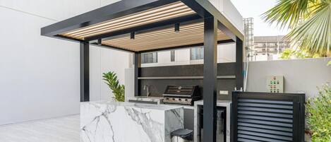 An outdoor kitchen with a marble countertop, a grill, and a pergola structure.