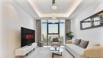 A modern living room with a large flat-screen TV, a sofa, a coffee table, and a city view through large windows.
