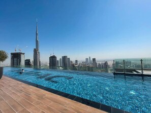 Una piscina infinita en la azotea con vistas al horizonte urbano, incluyendo un rascacielos destacado.