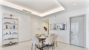 Zona de menjador moderna amb una taula rodona preparada per a quatre persones, envoltada de cadires. Una prestatgeria de vidre amb objectes decoratius es troba a l'esquerra.