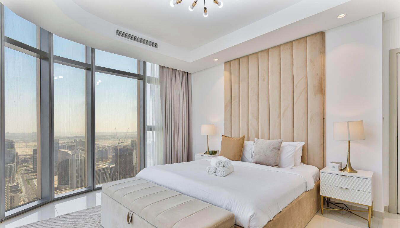 A modern hotel room with a large bed, a view of the city, and a cityscape visible through the windows.
