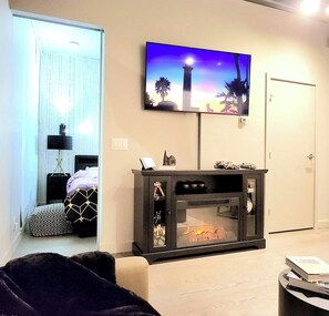 Een moderne woonkamer met een open haard, een flatscreen televisie erboven en een deur aan de rechterkant.