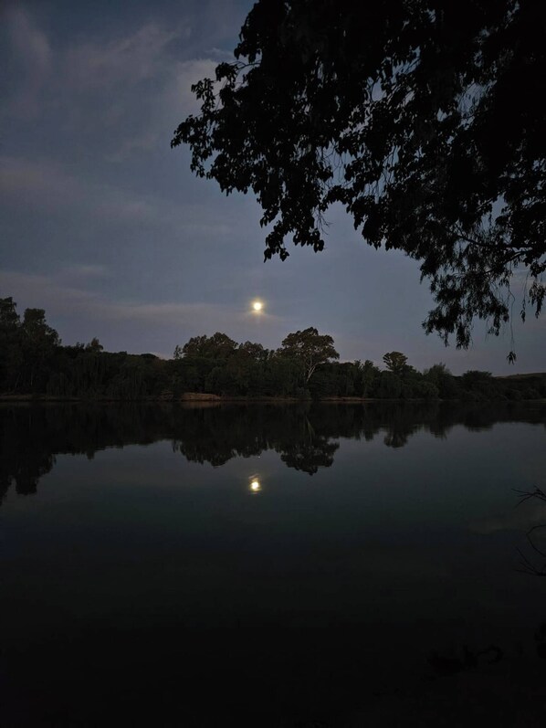 A calm lake at dusk with a visible moon reflection.