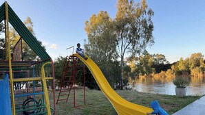 A playground with a yellow slide, a climbing structure, and a body of water in the background.